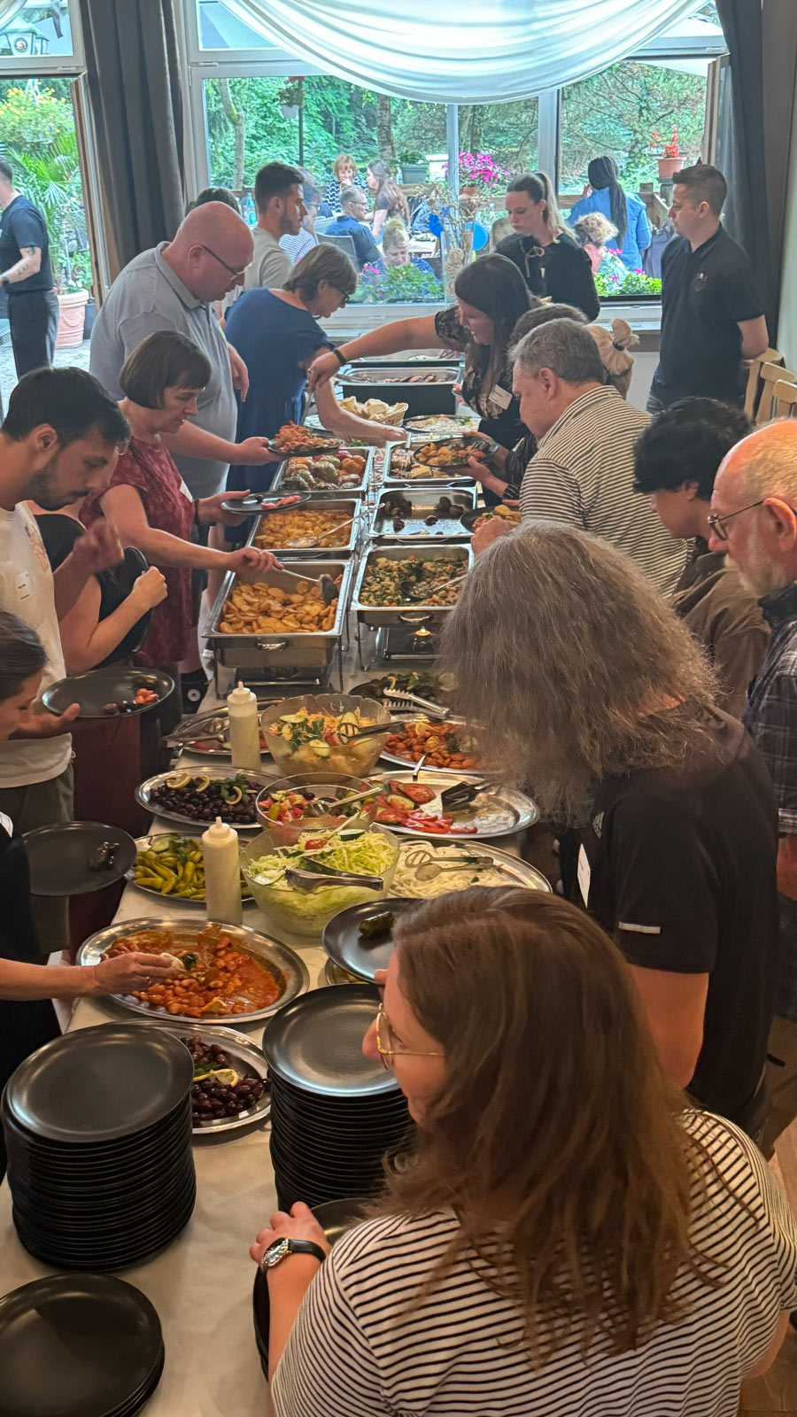 Mehrere Menschen stehen an einem Buffet mit buntem Essen, wirken fröhlich und gesellig